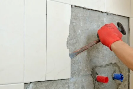 Person entfernt Fliese mit Hammer und Meißel